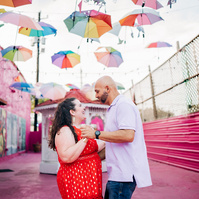 A newly engaged couple dancing under colorful umbrellas.