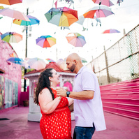 A newly engaged couple dancing under colorful umbrellas.