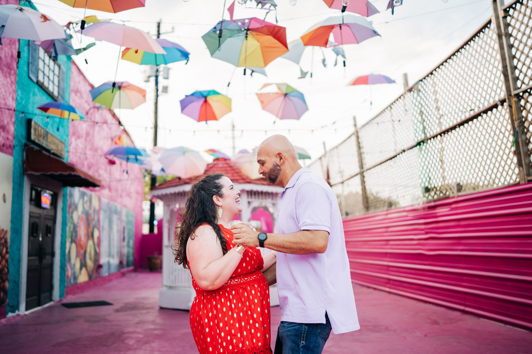 A newly engaged couple dancing under colorful umbrellas.