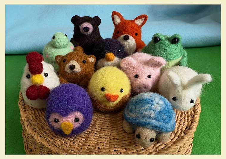 twelve tiny needle felt animals cozily gathered together atop a handwoven basket