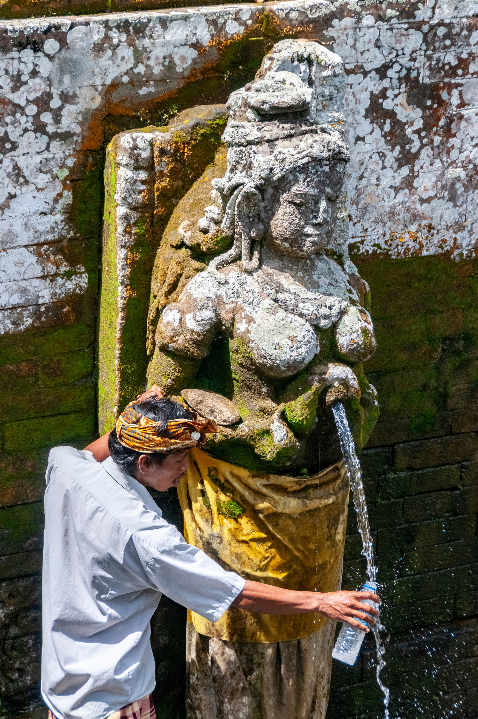 Man filling water bottle from ceremonial fountain at Goa Gajah Elephant Cave, Bali, Indonesia