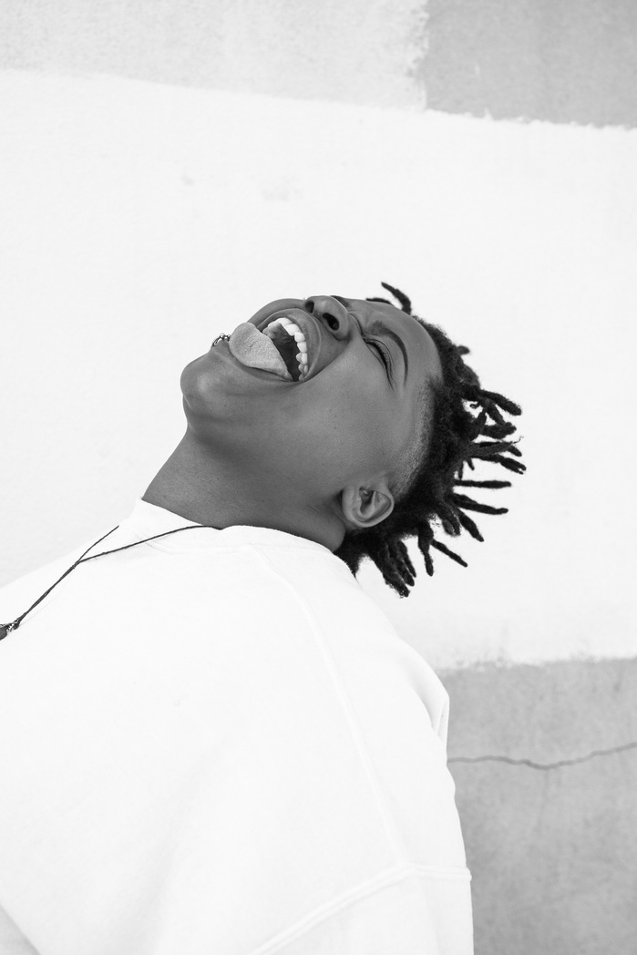 Monochromatic portrait of Mercury Music Prize winner Speech Debelle, shortlisted for Portrait of Britain Award Volume 6. Debelle, head tilted back, smiles freely with tongue out, embodying joy and liberation.