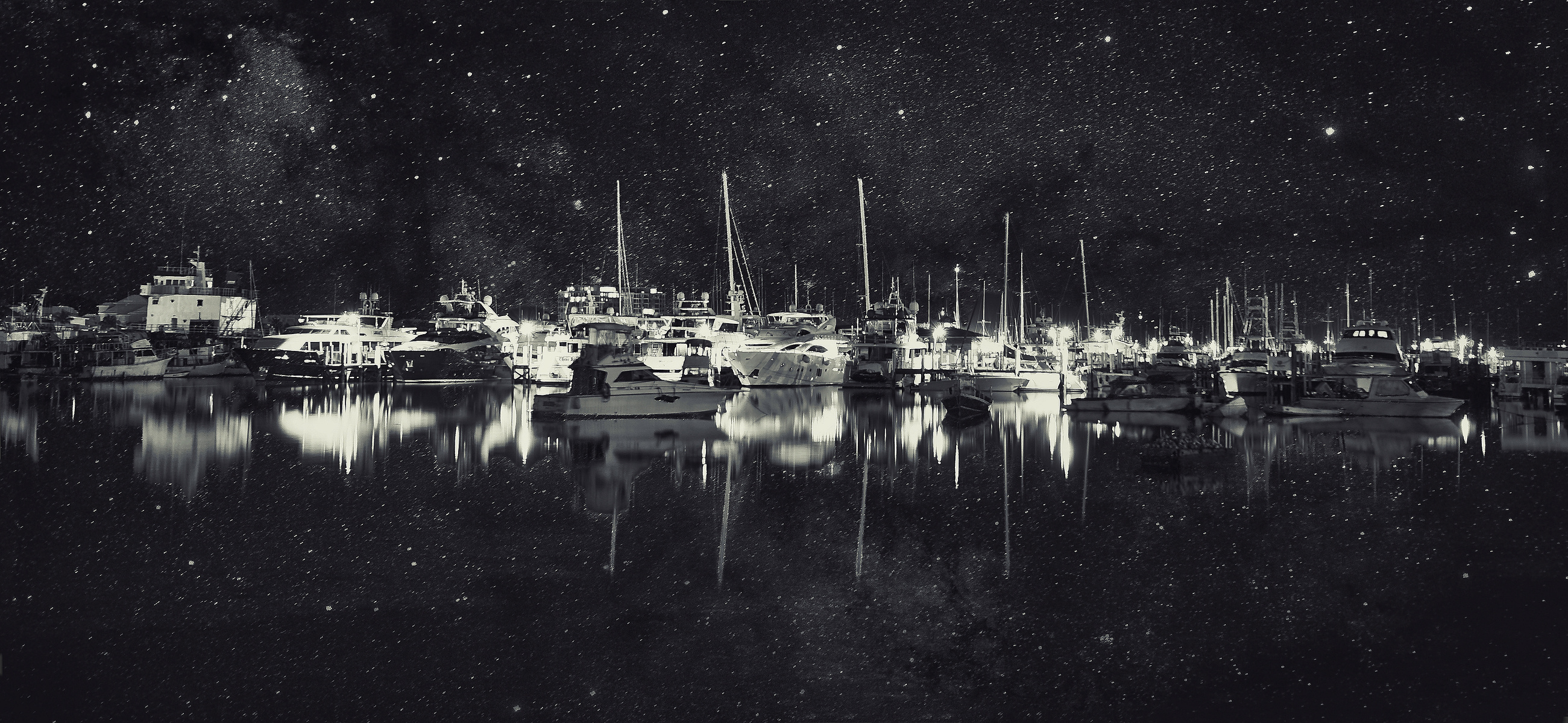 A stunning nighttime scene captures a marina with numerous boats reflecting in calm waters, under a star-filled sky. The combination of artificial lights and the natural glow of the stars creates a serene and mesmerizing atmosphere.
