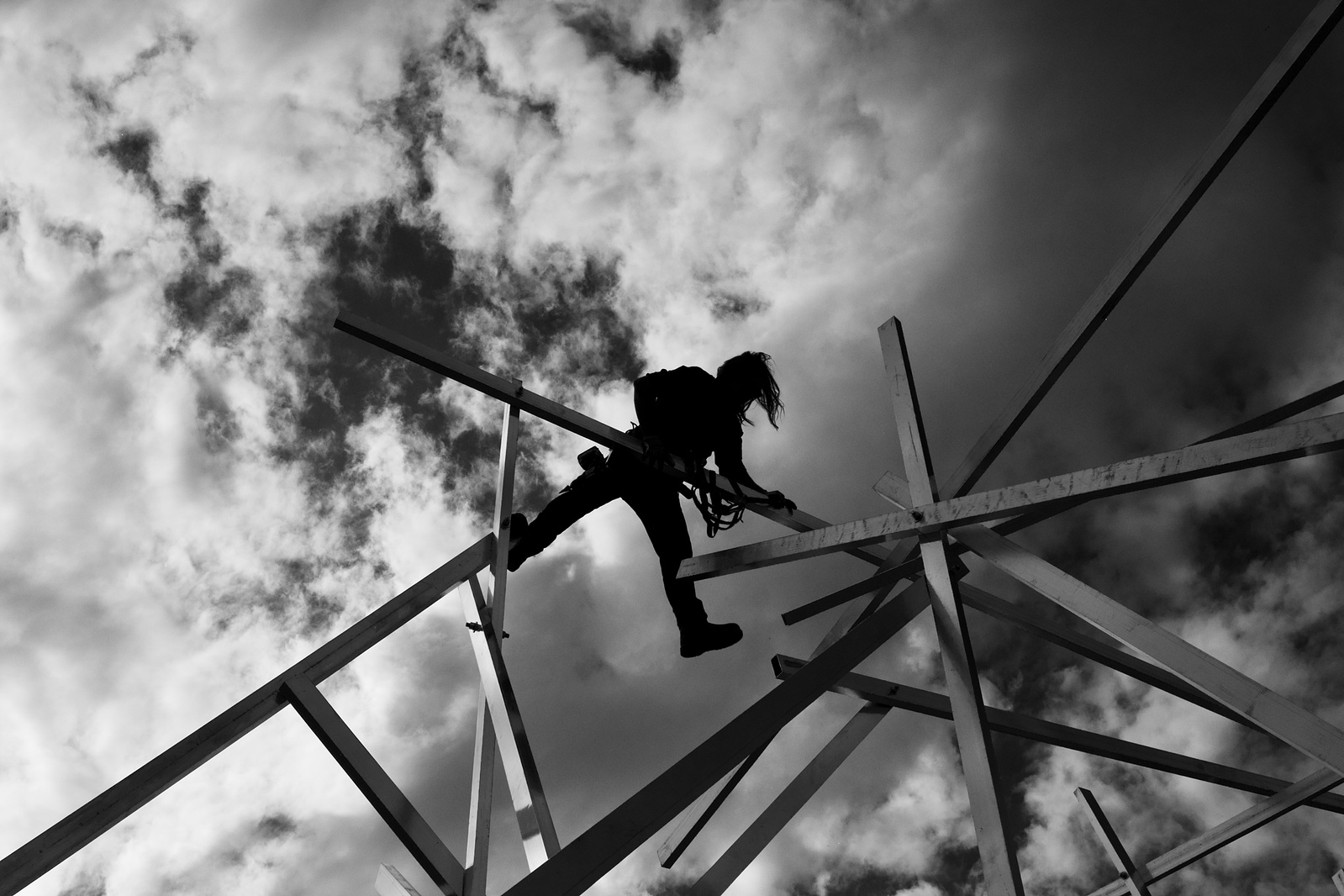 Matthew Gray climbing through radiating aluminum members of Mile Quartered beneath a clouded sky