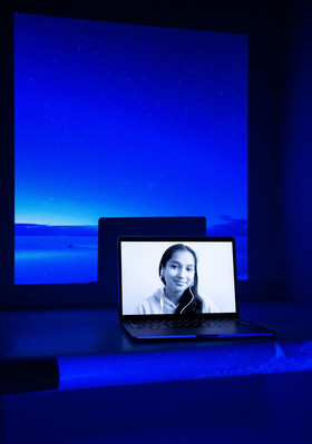 Digital portrait on a laptop screen with an image of a vibrant blue landscape with a few stars reflecting in the waterprojected into the background.