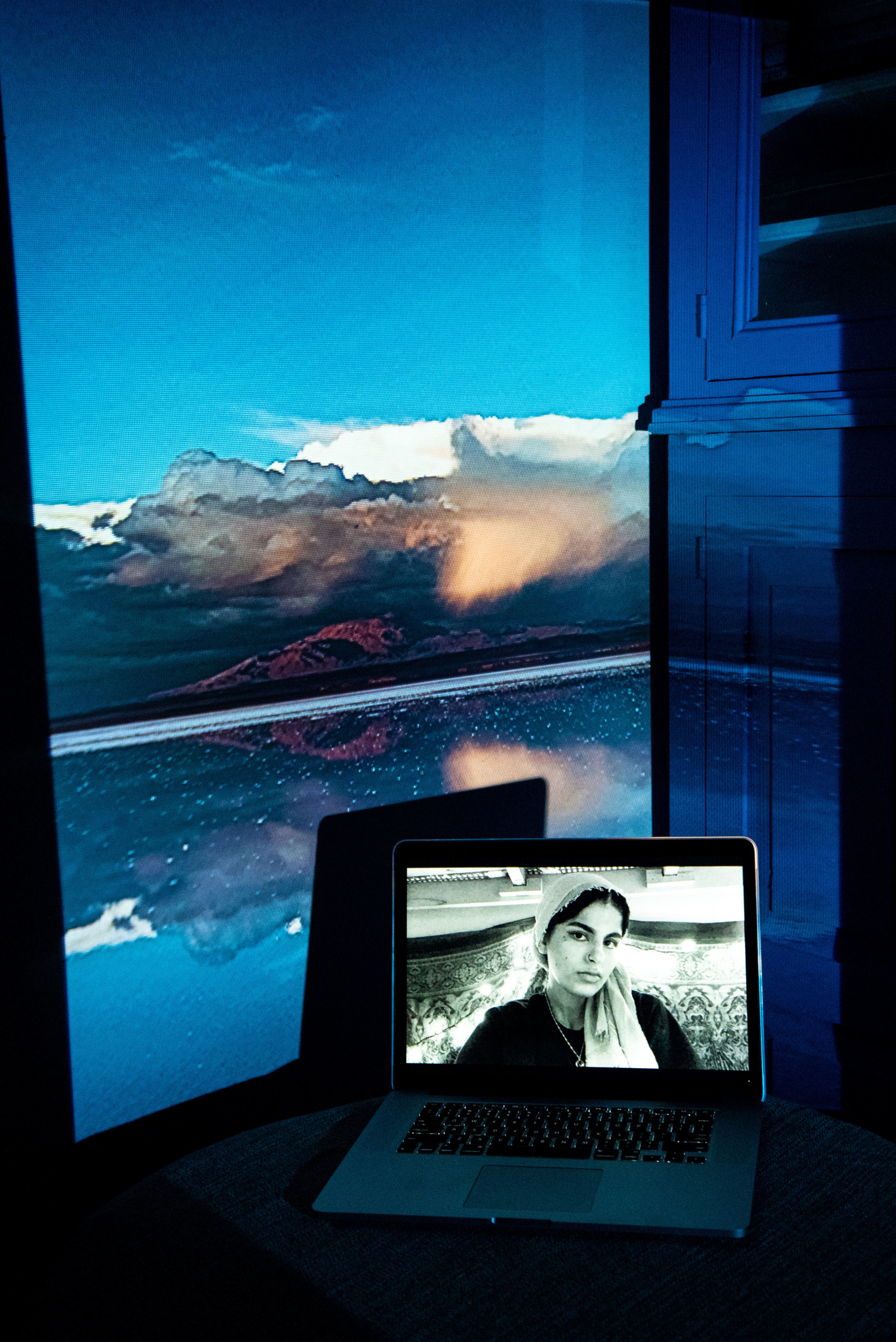 Digital portrait on a laptop screen with an image of a landscape with a mountain and cloud being reflected in a lake, projected into the background.