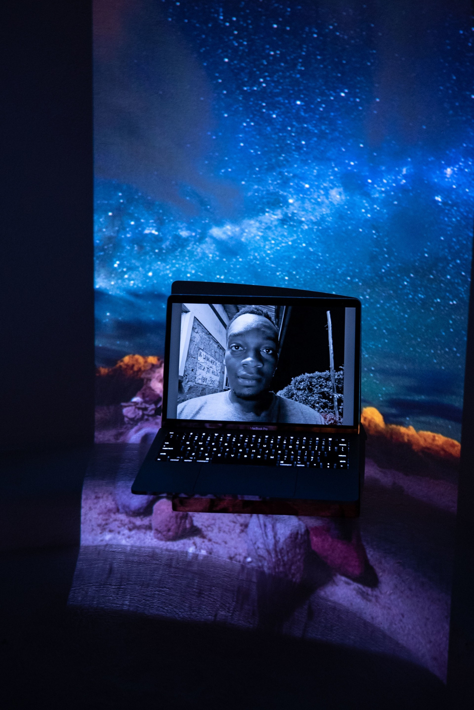 Digital portrait on laptop screen with an image of the Milkyway and prehispanic artifacts projected into the background.