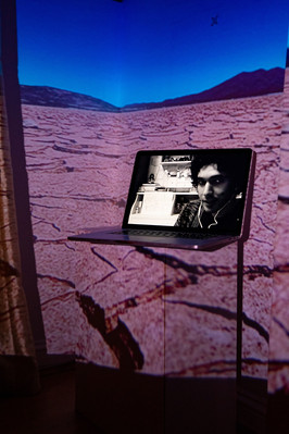 Digital portrait on a laptop screen with an image of a dried desert projected into the background.