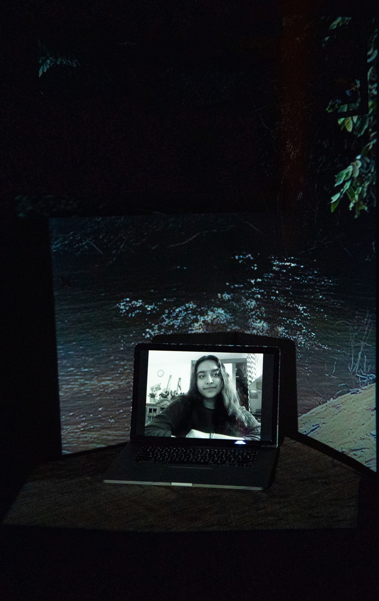 Digital portrait on a laptop screen with an image of a dark river projected into the background.