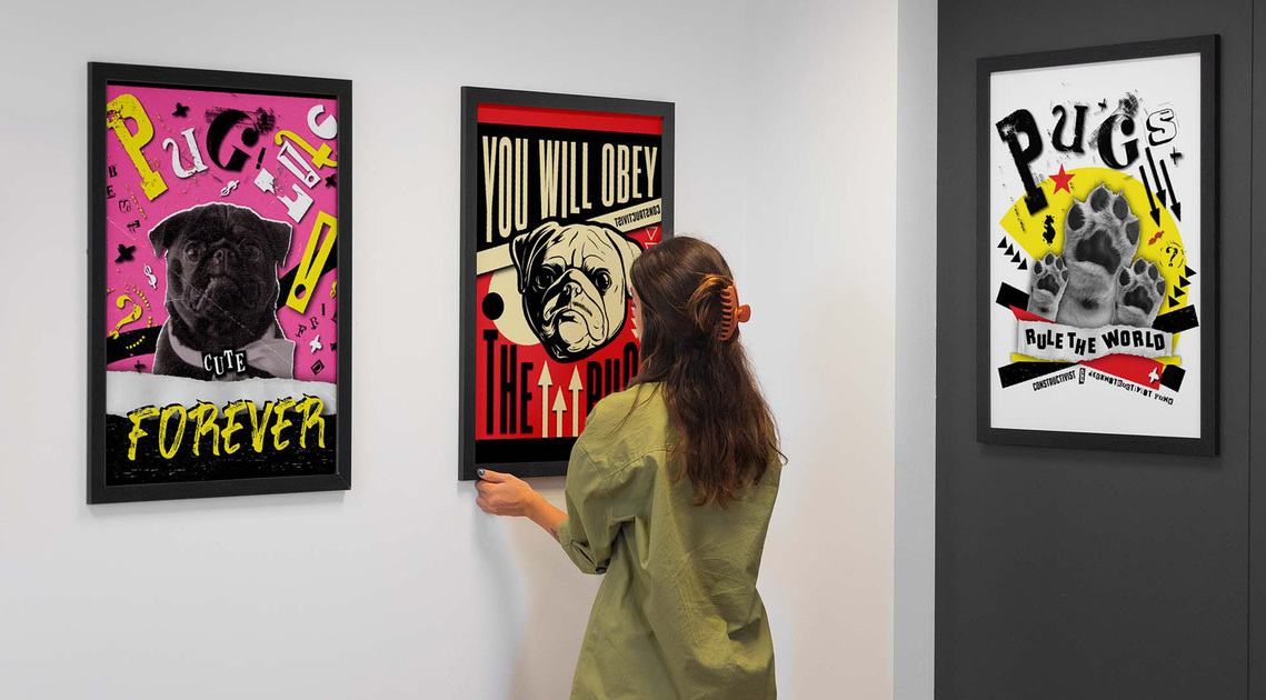 The image features a gallery wall adorned with the pug posters series, as a woman with long brown hair and a green shirt hangs one of the frames.