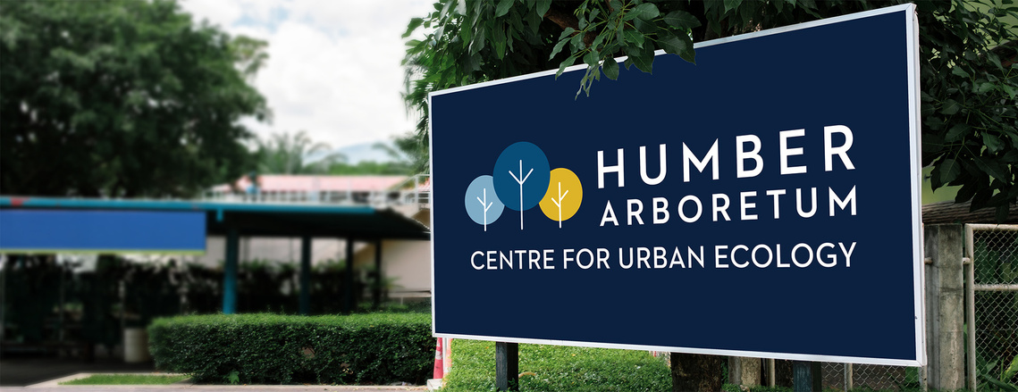 Image featuring a park entryway sign against a dark blue background with white text nestled in a bush, reading Humber Arboretum Centre for Urban Ecology.