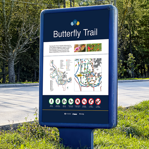 The image shows a large sign on the park pathway with the Humber logo, trail name, description, park map, and rules. White text and light blue arrows stand out on a dark blue background.