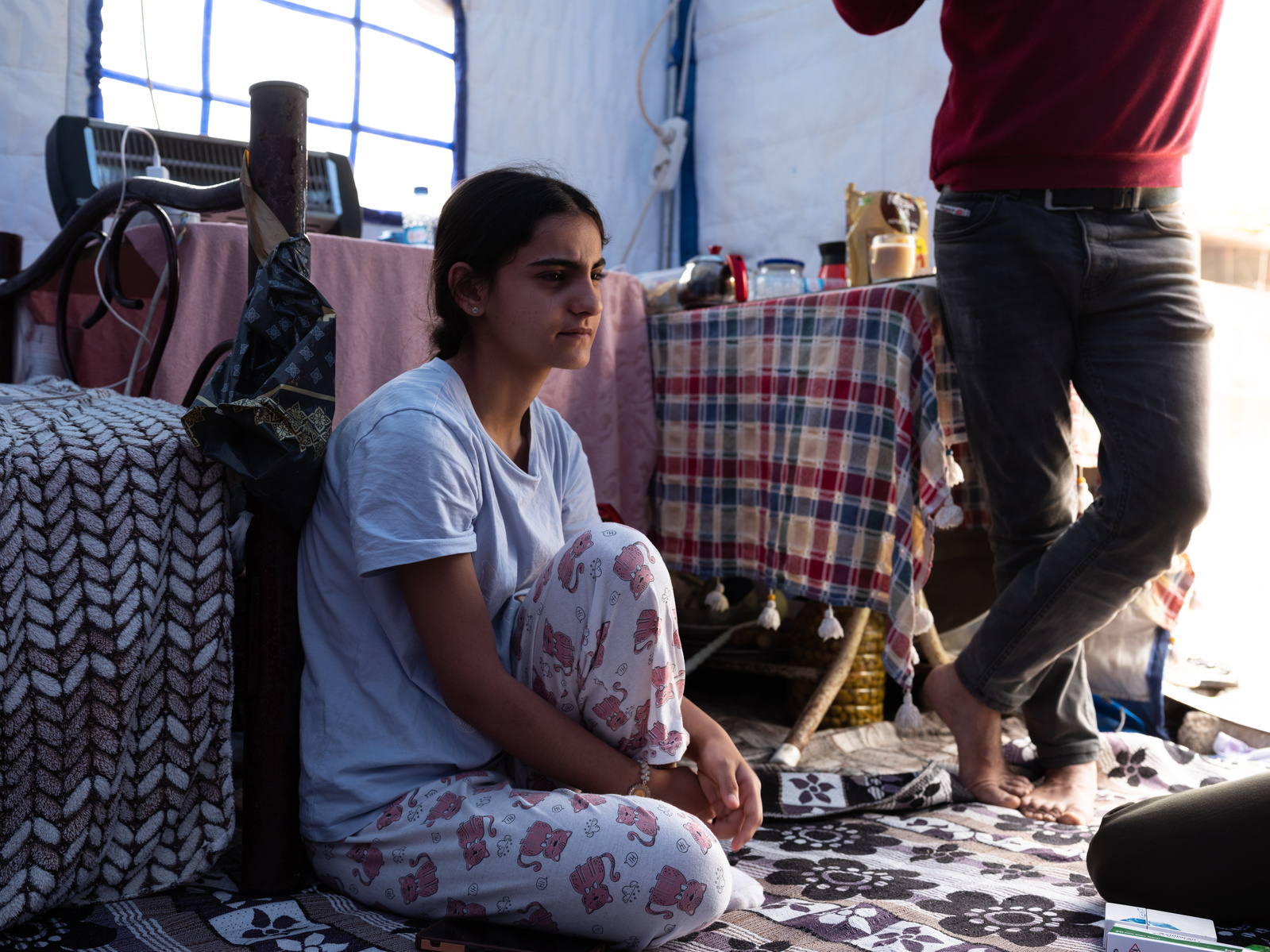 Rebiye Dogru sitting in her current tent home, next to her father Remzi (right) in the Haci Omer Alpagot neighbourhood of Antakya. After the multiple earthquakes damaged their home, they now live nearby in a tent camp alongside other homeless residents.