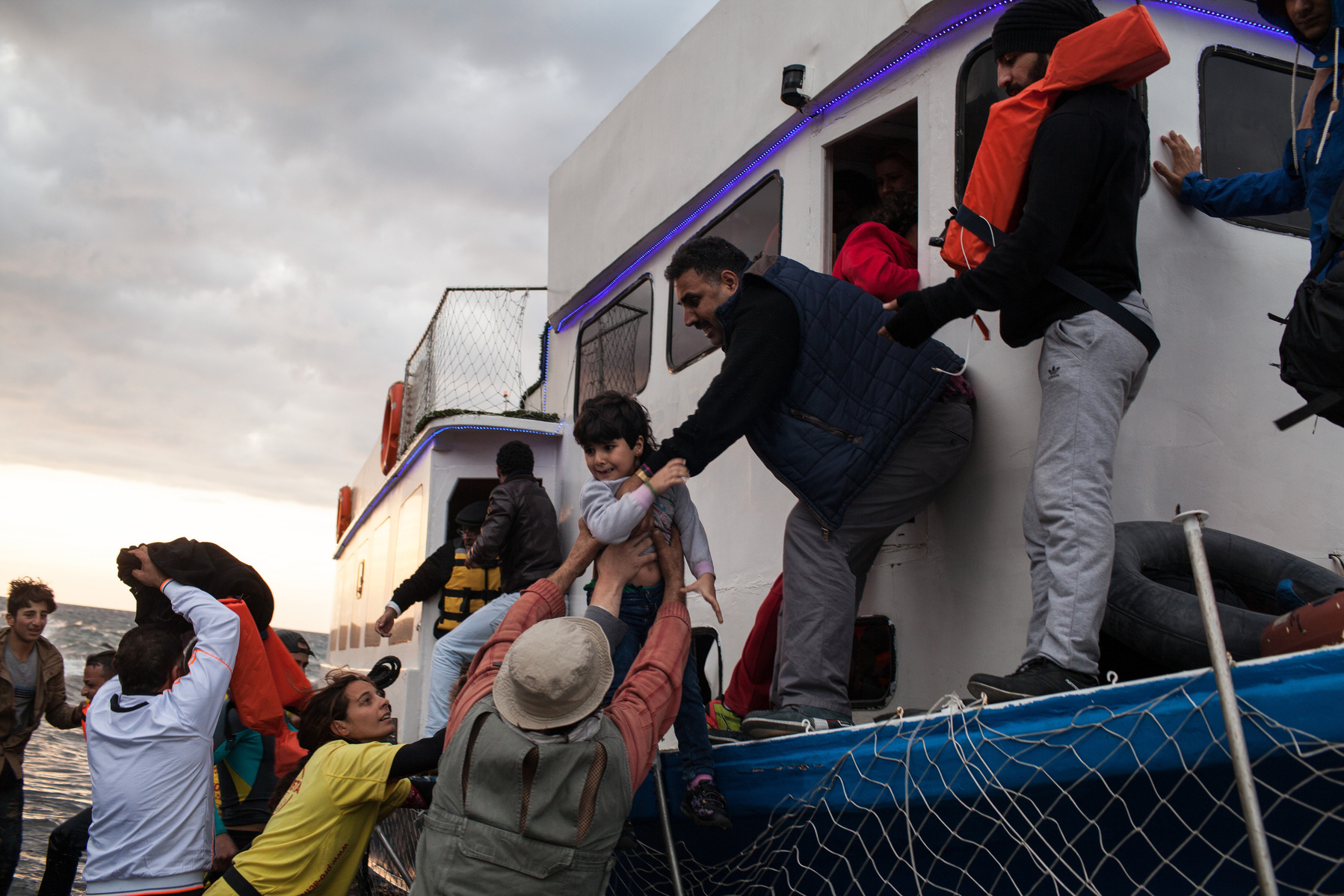 A boat carrying around 150 Syrian refugees lands on the Greek island of Lesvos. People are helped off by volunteers and other refugees.