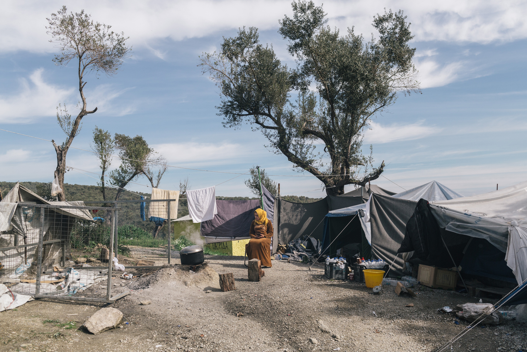 A female asylum seeker cooking on an open fire in the makeshift settlement next to the official Moria refugee camp site. Scattered amongst the olive groves, around 1500 people live in tents and shelters in this unofficial site.