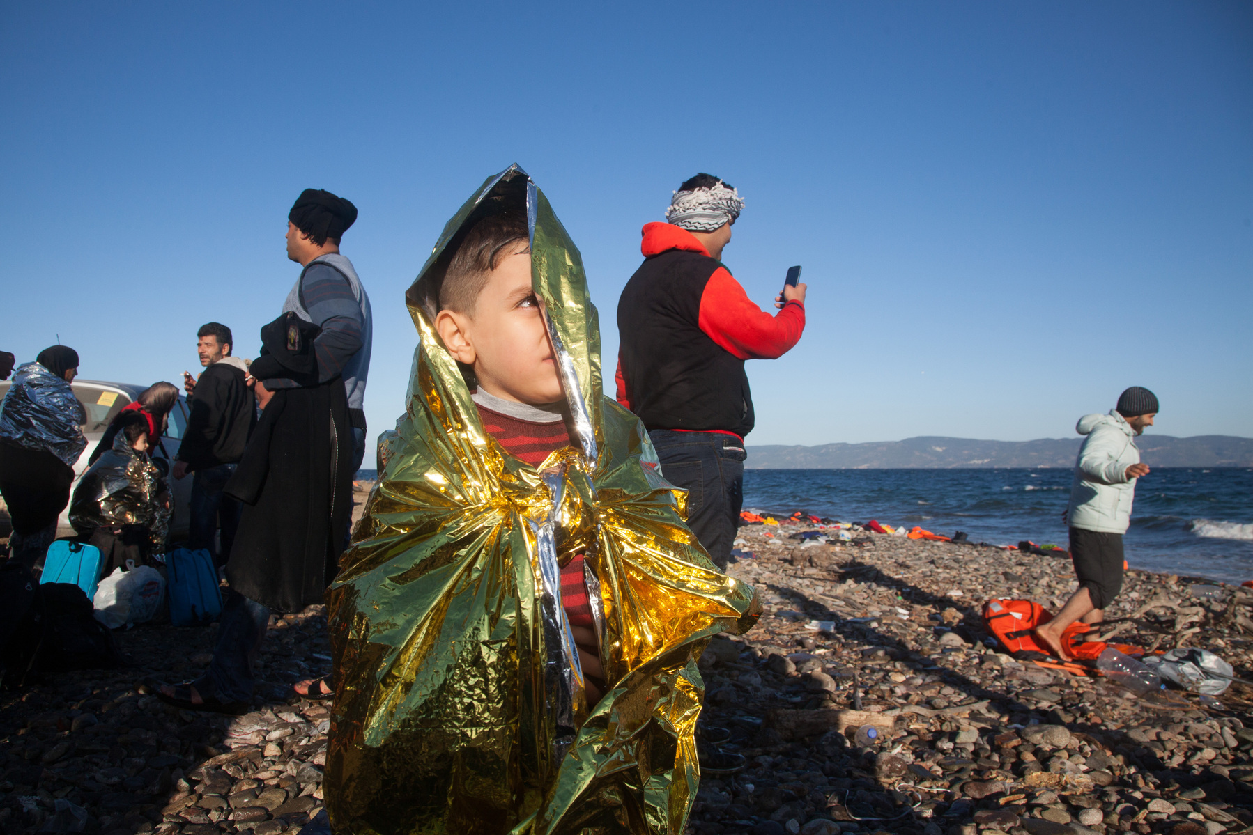 A Syrian boy stands on a beach near Molyvos, Lesvos island in Greece, wearing a foil blanket designed to prevent wind and create warmth.