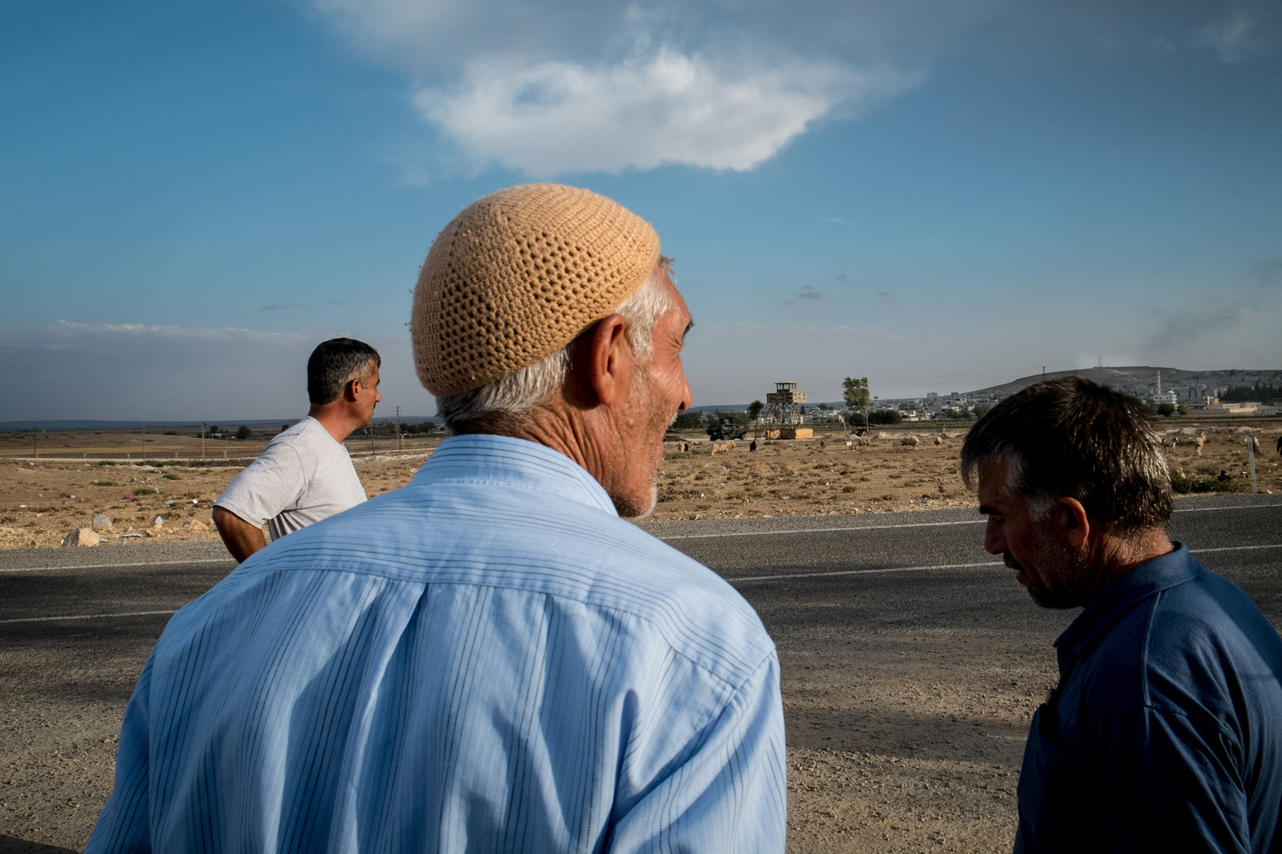 Syrians Kurdish men watch smoke coming from their hometown of Kobane/Ayn al-Arab (background right) from the Turkish side of the border near Suruç.