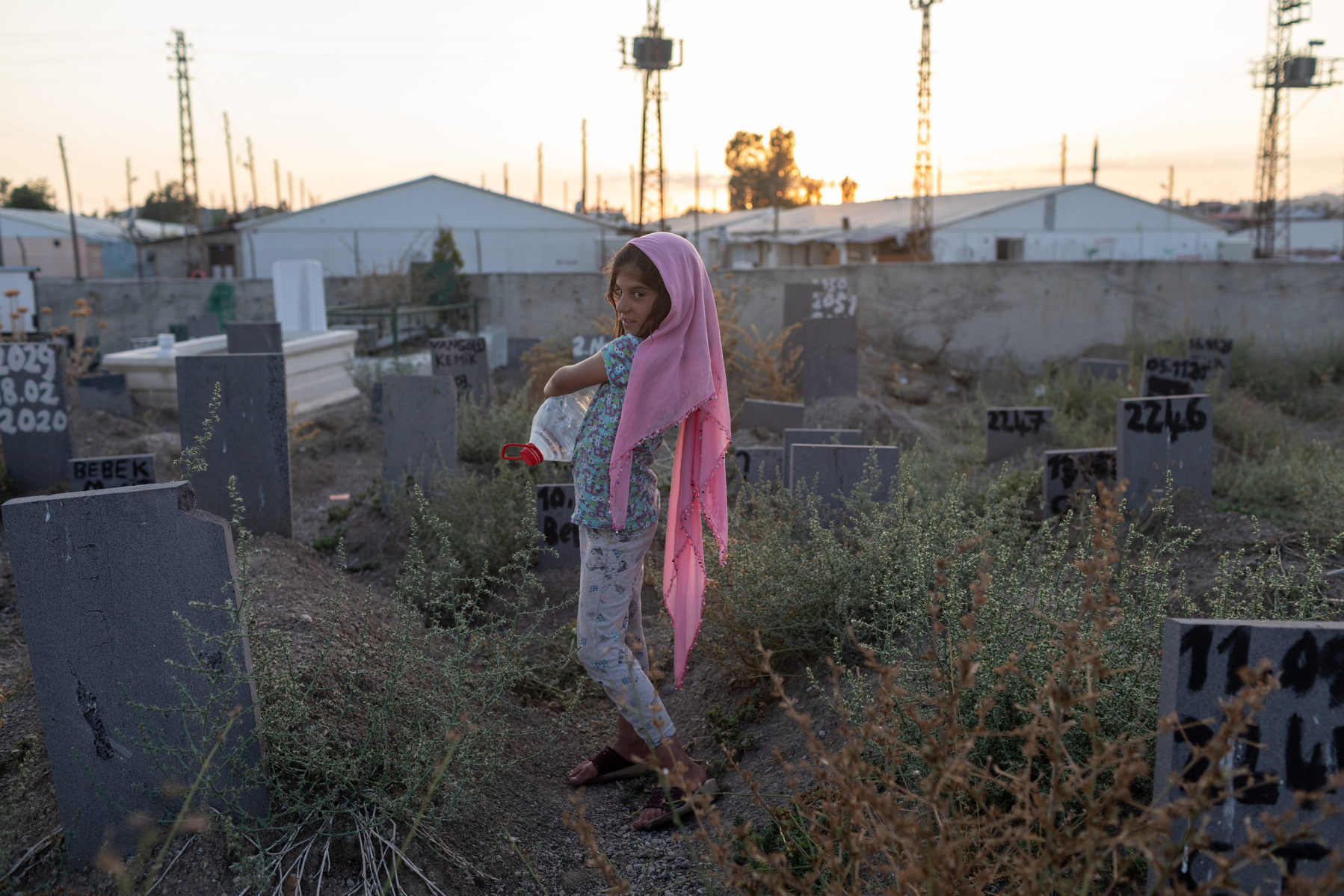 A graveyard in Van, Turkey, containing tens of migrant bodies, who's identities are unknown, and instead are listed as numbers. A young girl who lives nearby offers to sell water to those visiting the graves.