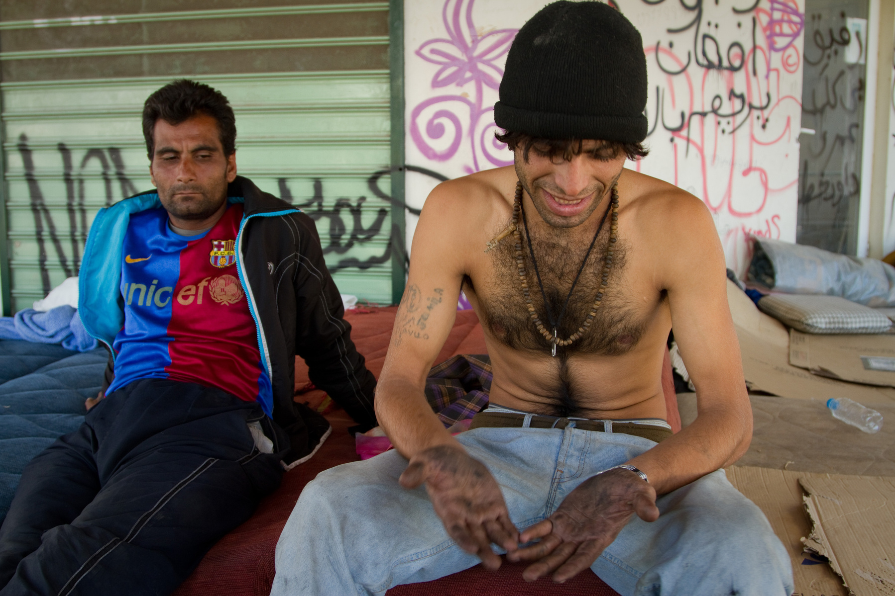 Sitting in a park where they sleep, two men from Pakistan and Afghanistan return from the port in Patras where they were unsuccessful in smuggling themselves onto Italy.