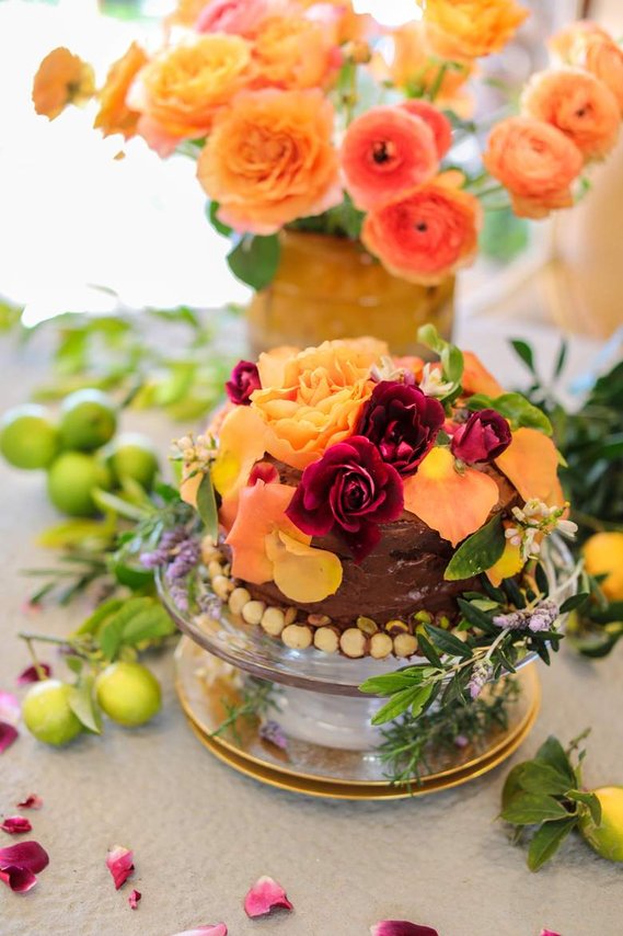 A chocolate olive oil cake decorated with pistachios and macadamia nuts. Covered in vibrant roses. 