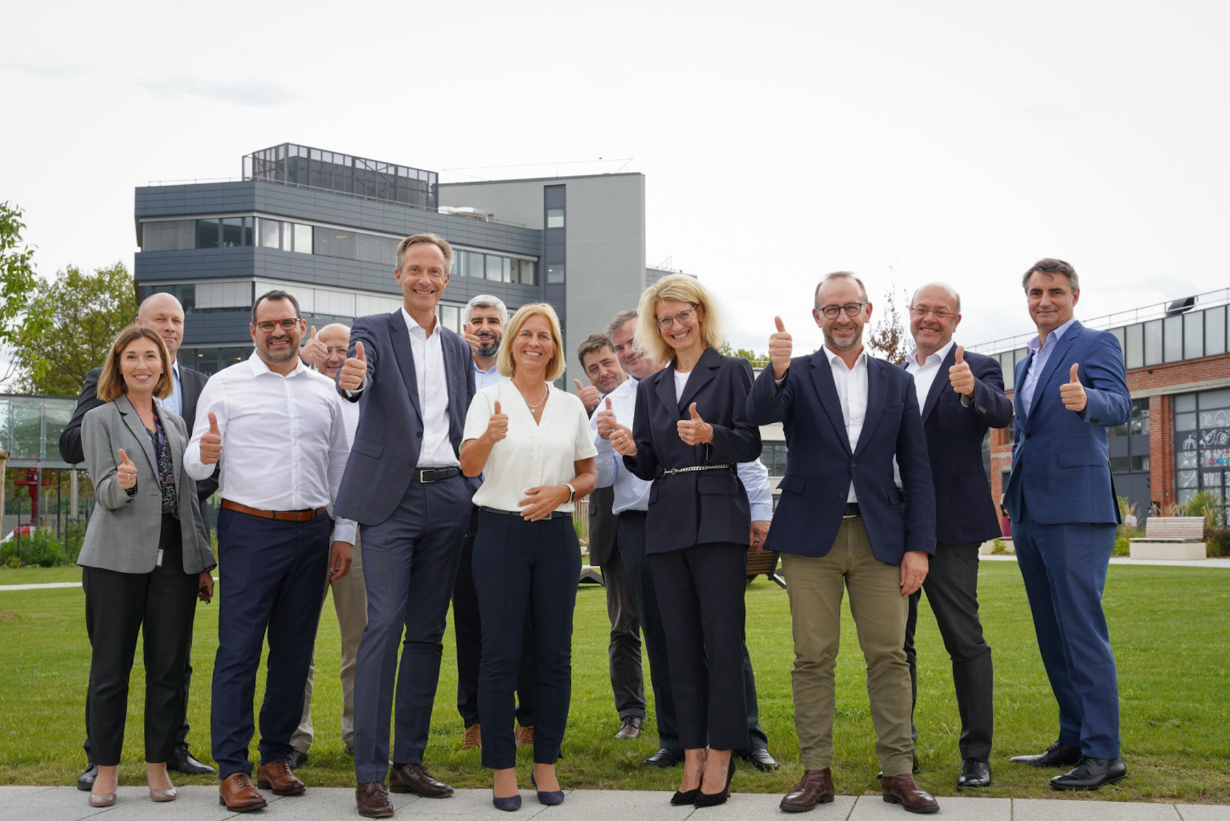 n groupe de dirigeants corporate d’une société internationale pose avec enthousiasme, tous souriants et le pouce levé, reflétant leur esprit d’équipe et leur succès partagé dans une ambiance conviviale et dynamique.