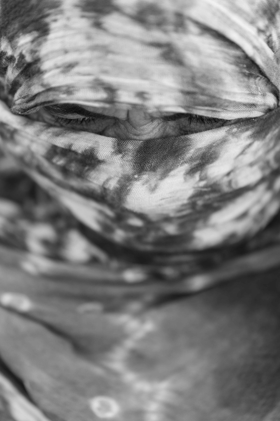 Une femme nomade du Sahara, enveloppée dans un foulard qui laisse entrevoir une ligne de rides et ses yeux perçants, témoigne de la dureté de la vie dans l’immensité aride du désert.