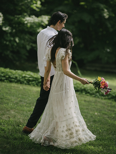 Elopement couple walking toward a lake in Warren, Connecticut holding flowers — captured by a CT-based wedding photographer.