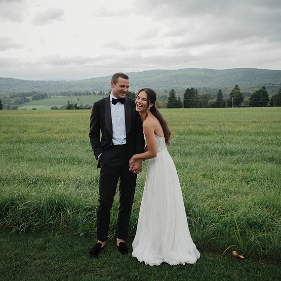 Couple in a field at Lion Rock Farm in Sharon, Connecticut with Berkshire Mountains in the background under gray skies — captured by a CT-based wedding photographer.