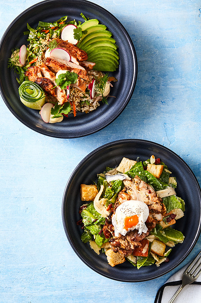 A chicken caesar salad and burrito bowl photographed on a blue white textured background. Photographed by a professional food photographer for a business menu photography.