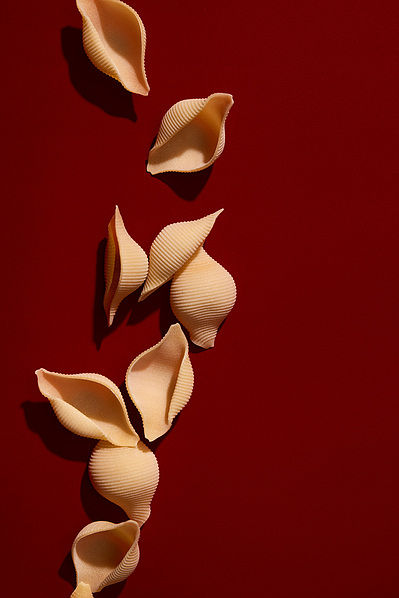 High contrast image of conchiglie pasta sitting on a deep red background with hard flash lighting resembling high noon