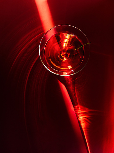Advertisement photography of golden hour light ray falling on red background with a martini glass on top. Light rays reflecting from the glass forming spiral shapes and reflecting beautifully on a dark red background
