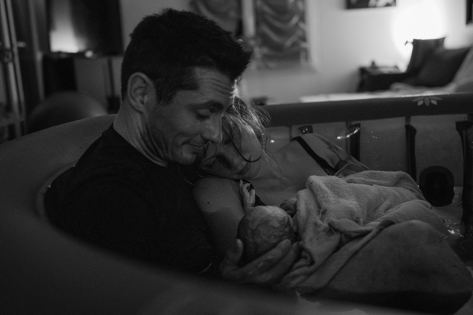 Un couple de jeune parents sont dans les bras l'un de l'autre et accueillent leur nouveau né.