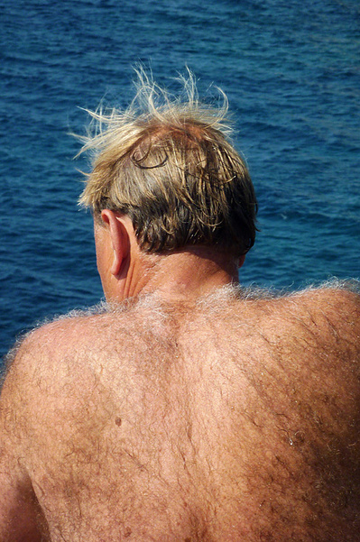 Señor peludo con el torso desnudo y el pelo al viento con el mar de fondo David Salcedo