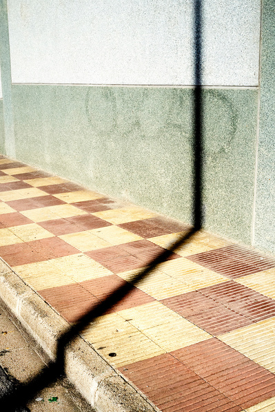 Sombra de farola proyectada sobre los baldosas rojas y una pared azul David Salcedo