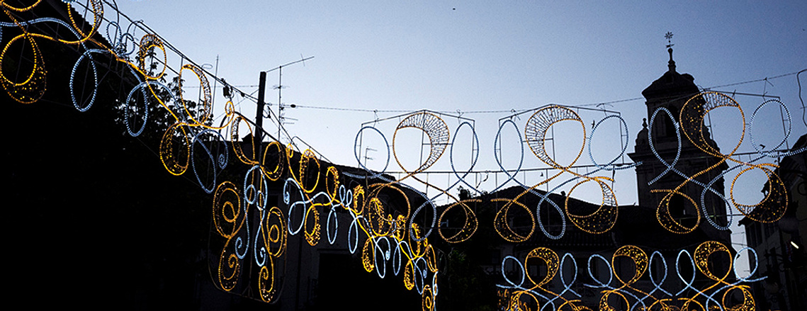 Luces de feria iluminadas al amanecer con un campanario de fondo David Salcedo