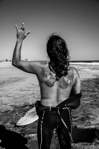 a surfer guy throwing a shaka, or &quot;hang loose&quot; sign, while shopwing off his back tattoos. The tattoo has guitars, a woman, and a tribal insignia