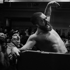 Michael Mistretta taking a chop across the chest. his face is twisted in pain. In the background an obese fan reacts, NYWC Feb 2022