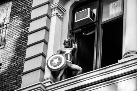 Black and white photo of a latino man dressed as Captain America on a buildings ledge during an Occupy Wall Street March