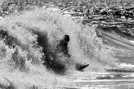 a black and white photo of a surfer encapsulated by a wave