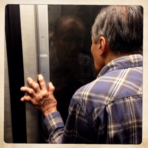An Asian man with crooked fingers looking forlornly out of a subway window 