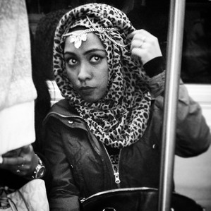 A pretty woman with glowing eyes adjusting her headscarf on the New York City subway