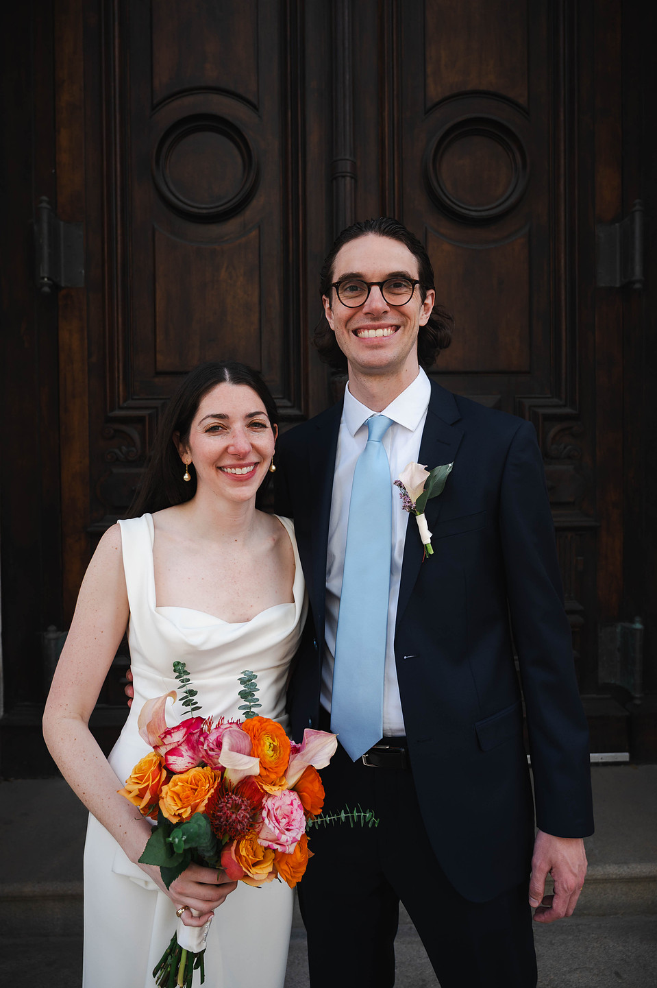 Bride and groom standing in front of the dark brown doors of the Tweed Courthouse in NYC