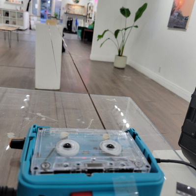 A depth shot from the listening station, it is a blue, modified tape walkman with a modified cassette with ferrous tape extending to the front of the room