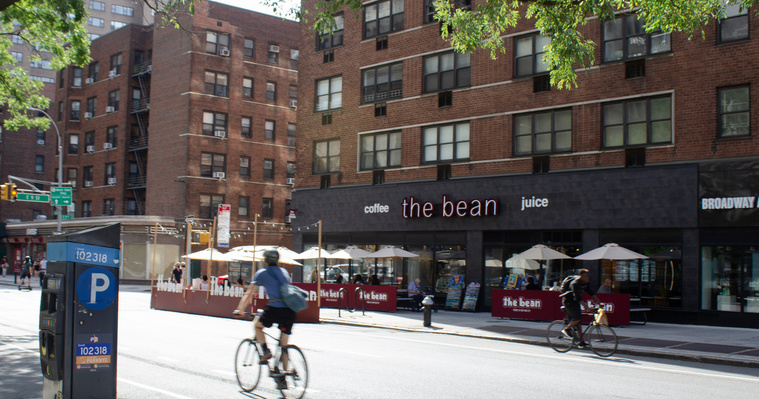 The Bean, coffee shop in Manhatten, NYC. Location street photography by Vermont-based Artist and Photographer, Kevin Michael Smith. Photo of cyclists and people passing by outdoor patio seating. 