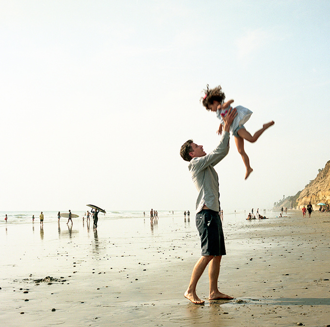At he beach a father throws his young daughter in the air and catches her.