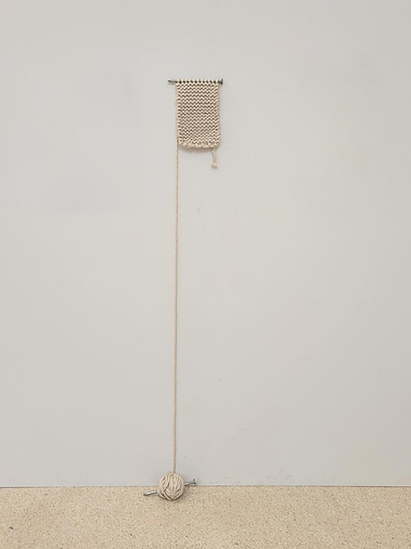 a half complete knit scarf on oversized nails; the remaining yarn rolling down to the ground.