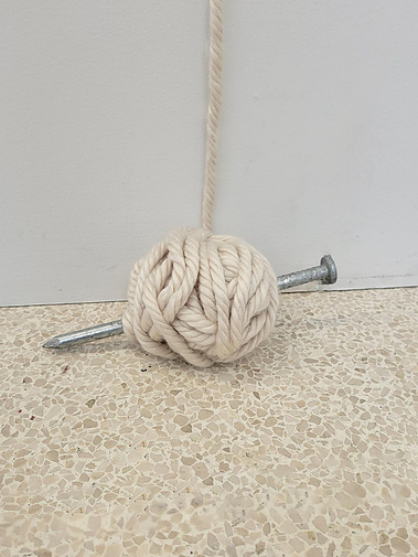 detailed photo of the ball of yarn. a oversized steel nail (knitting needle) pierced through it.