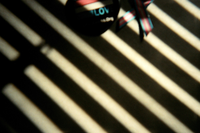 A trans button and trans flag poke halfway into the top of the frame. The rest of the frame is made up of alternating stripes of white light and black shadow.