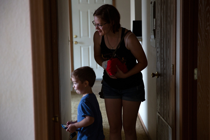 A woman and young child stand in a hallway and look into a room.
