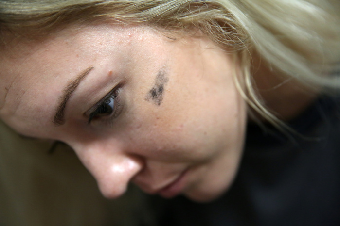 A woman looks intently out of frame. A smudge of black paint is on her cheek.
